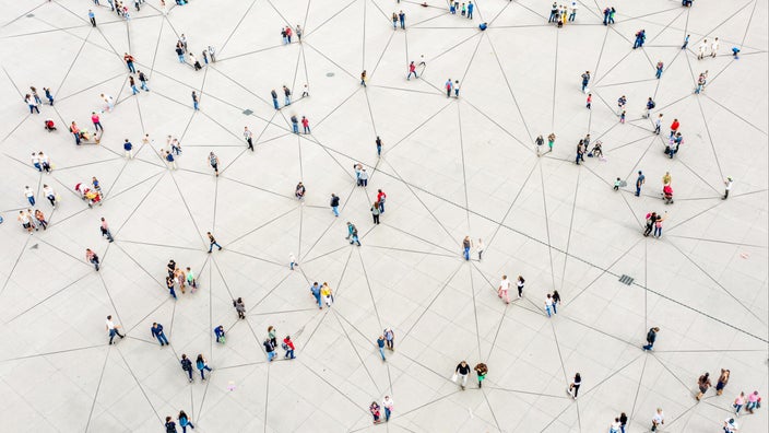 Aerial view of a scattered crowd of people. There are lines on the ground creating geometric triangles that look like lines connecting the dots of the people. 