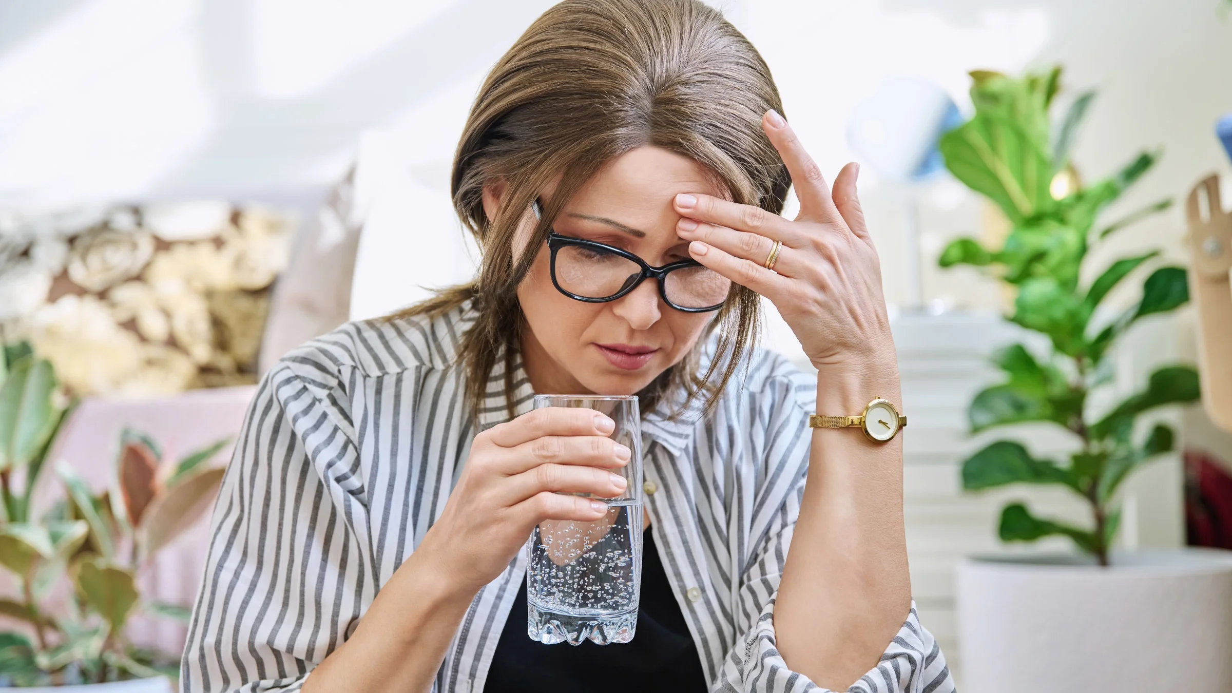 A woman experiencing a headache and holding a glass of water.