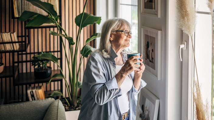 An older woman is drinking a cup of coffee at home. Research shows that coffee consumption is associated with a lower risk of developing kidney disease.
