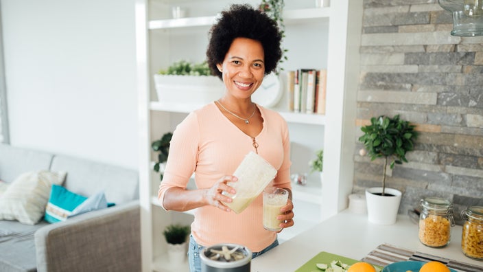 Woman pouring her smoothie into a cup. She is smiling and looking at the camera.