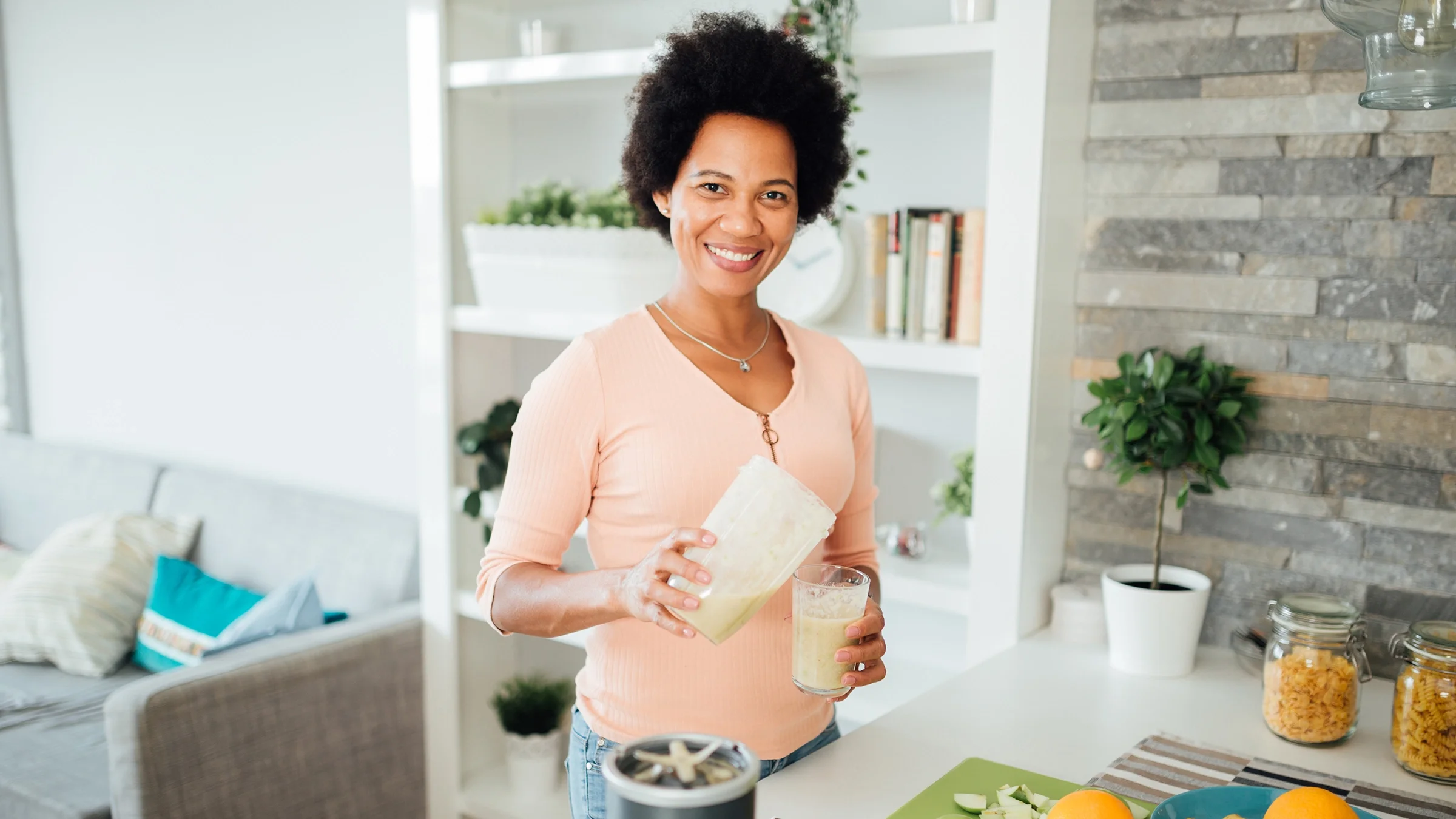 Woman pouring her smoothie into a cup. She is smiling and looking at the camera.