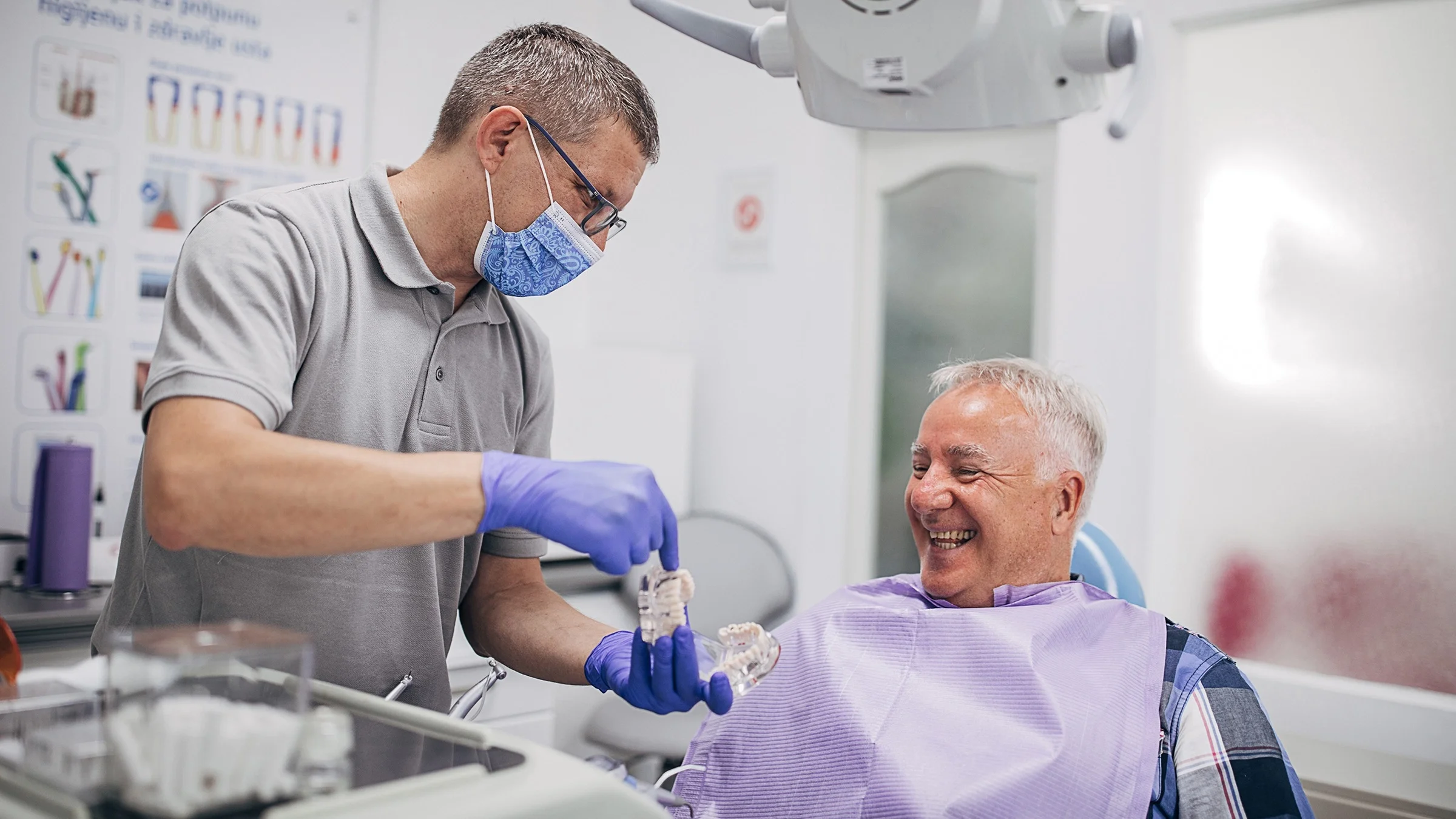 A senior man in the dentist chair smiling as his dentist explains denture work to him.