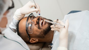 Health: dental care: man smiling while dentist examines teeth-1302979710