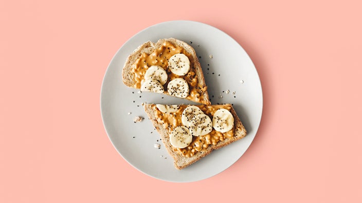 Peanut butter banana toast on a white plate with a pink background.
