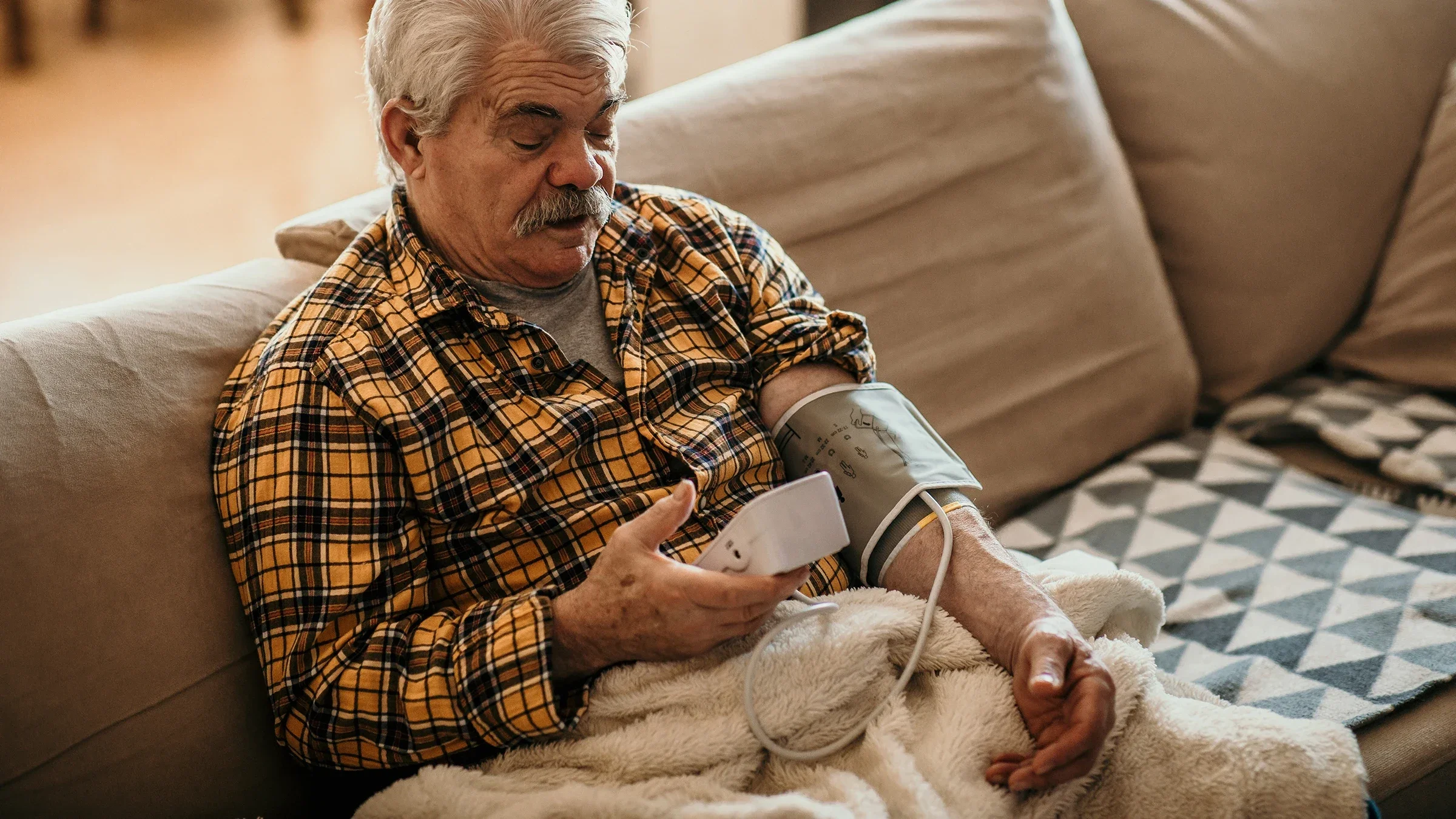 Senior man taking his blood pressure on the couch.
anandaBGD/iStock via Getty Images