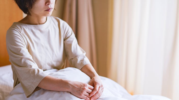 A woman sits in bed with a blank expression on her face.