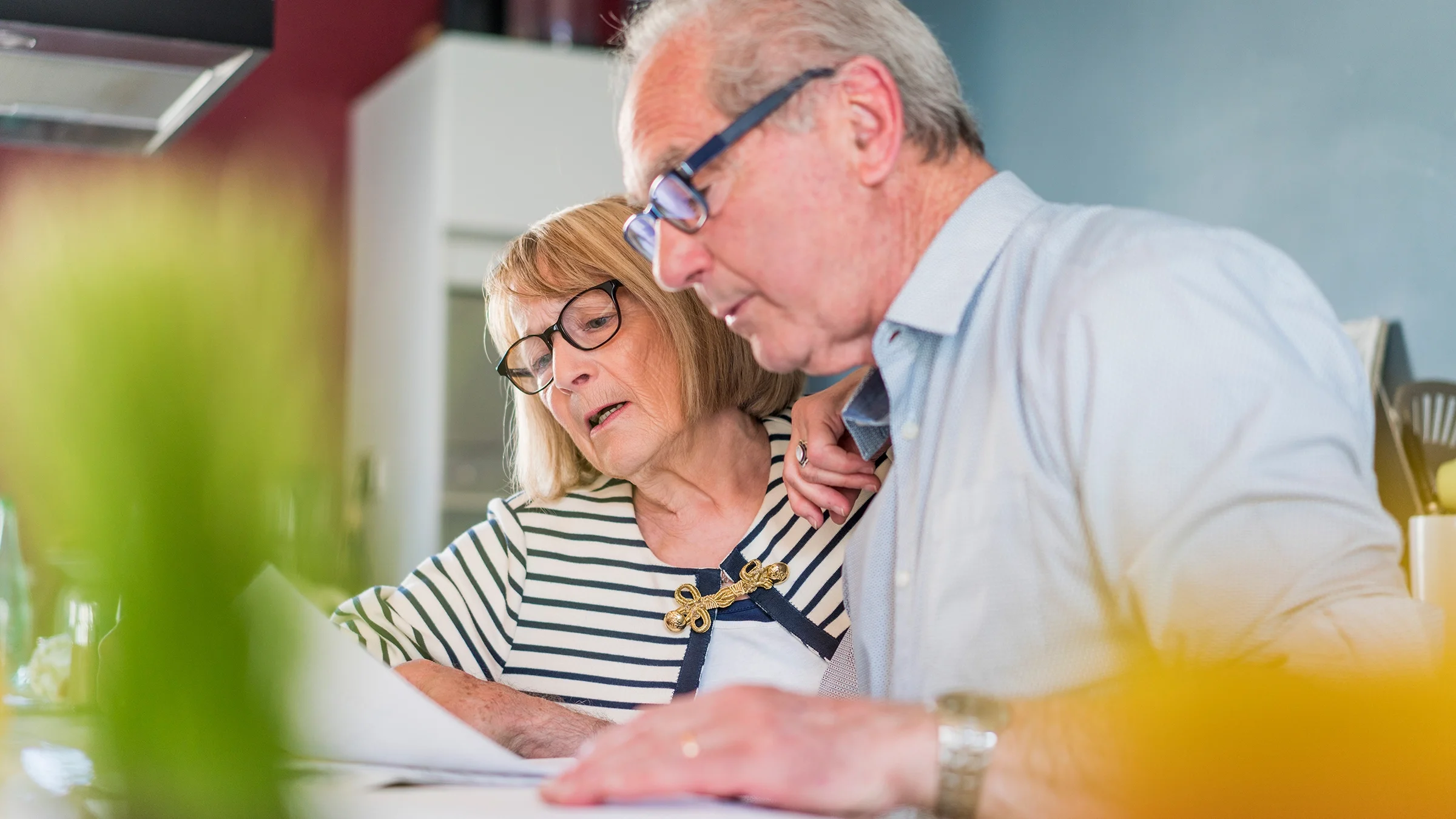 An older couple is reviewing paperwork at home.