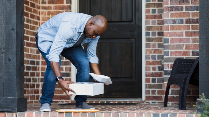 A man picks up packages from the front porch of his home.