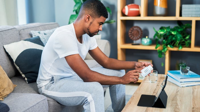 A young adult holding a pill bottle and looking it up on a tablet.