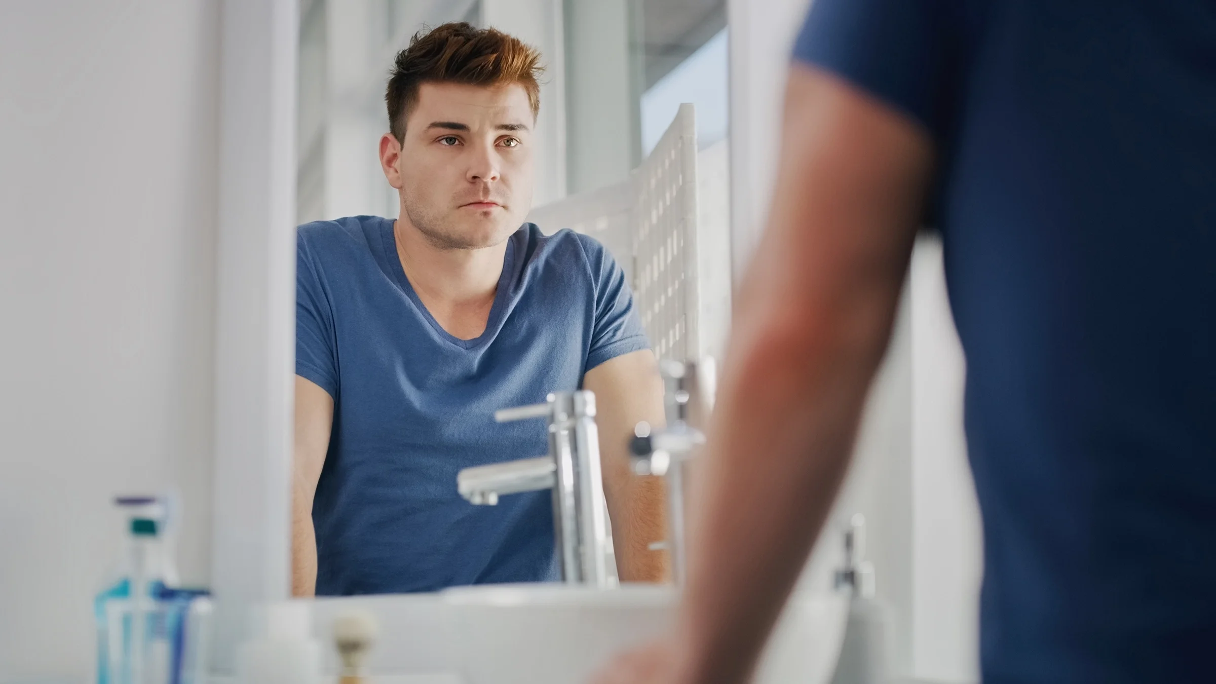 A man is staring into the bathroom mirror, looking upset.
