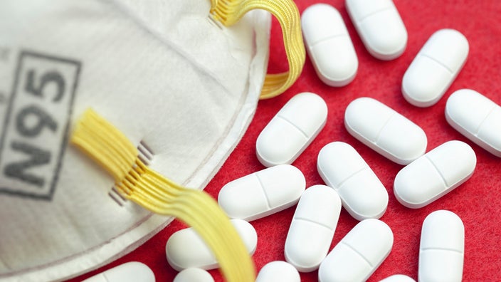 Close-up on a pile of white oblong pills and a N95 mask on a red background.