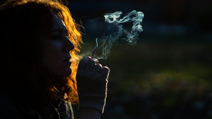 A woman smokes a cigarette at the park.