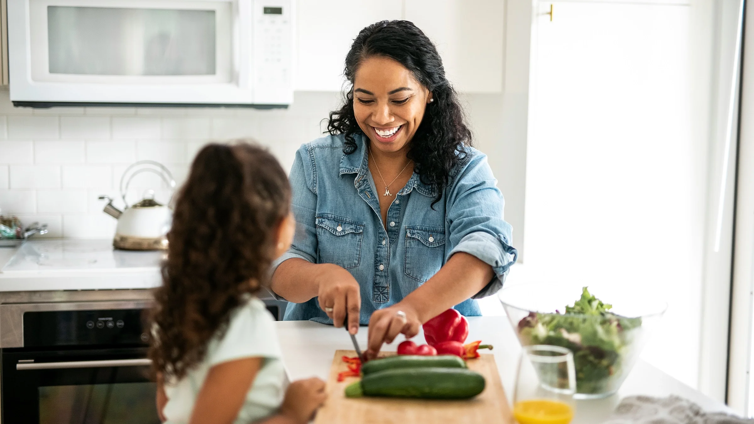 A mother and daughter cut vegetables in the kitchen.