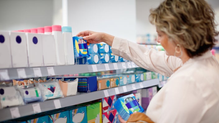 A woman takes sanitary pads from the shelf in a store.