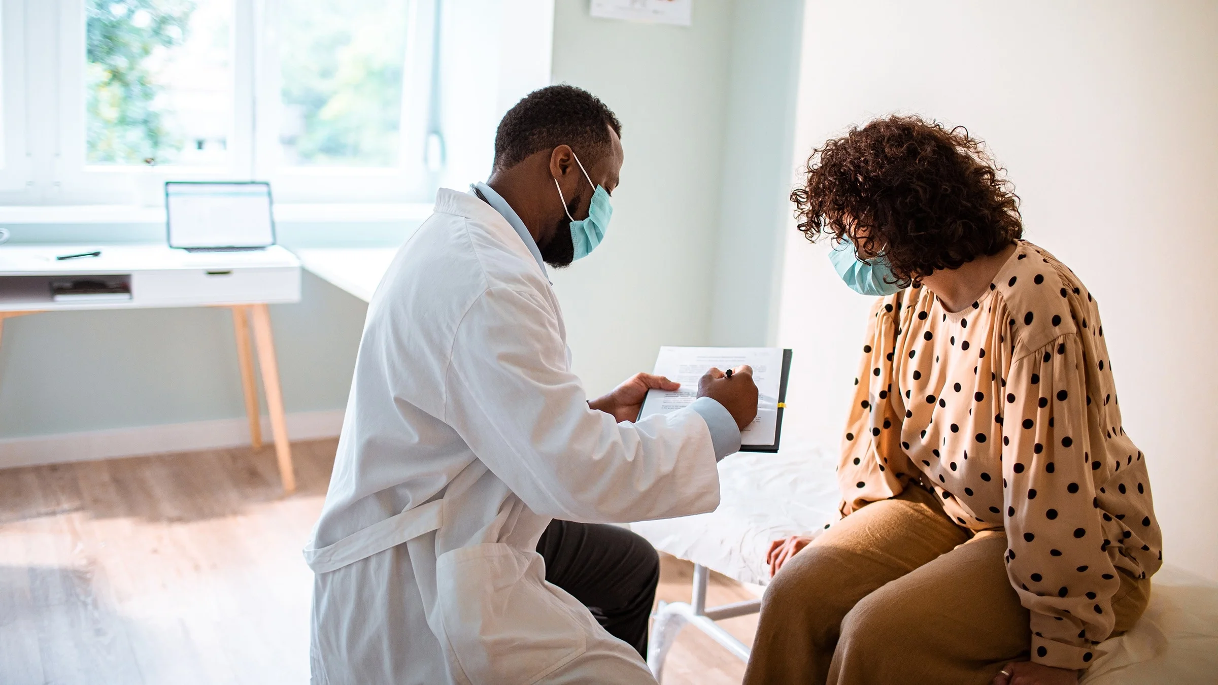 Male doctor showing female patient medical documents on clip board in an exam room