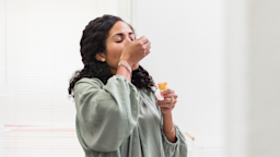 Woman closing her eyes and tilting her head back as she takes her pills from an orange prescription bottle.
SDI Productions/E+ via Getty Images