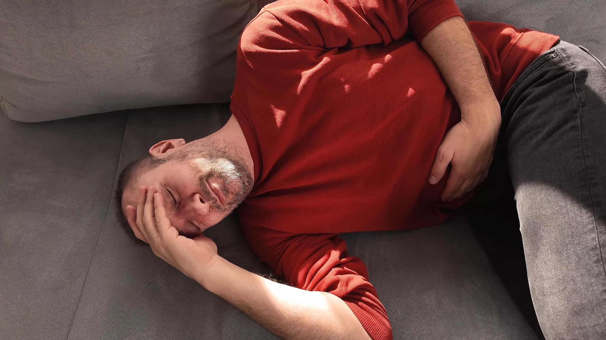 A man with abdominal pain lies on a couch holding his stomach.