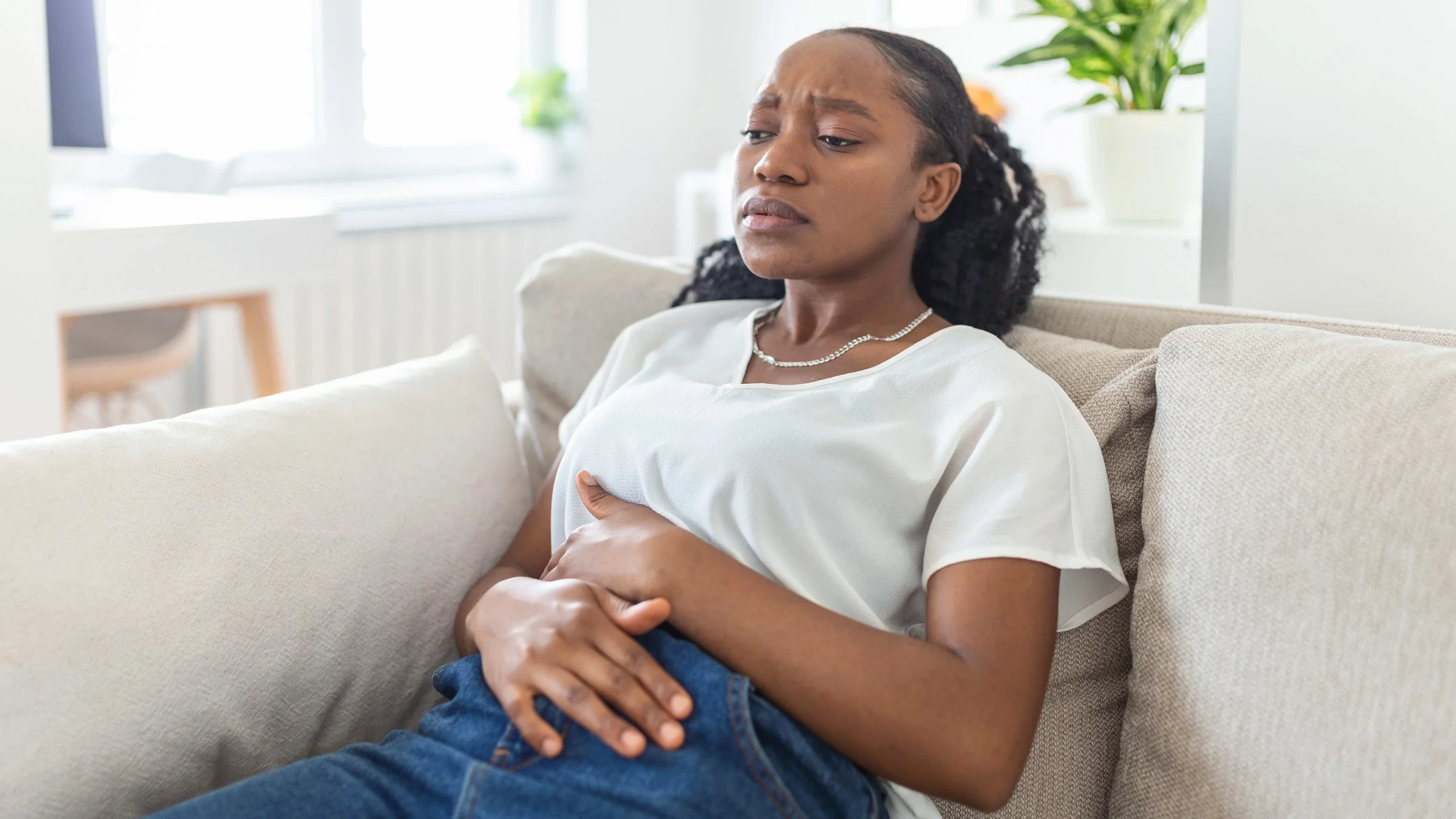 A bloated person sitting on a couch and holding their stomach.
