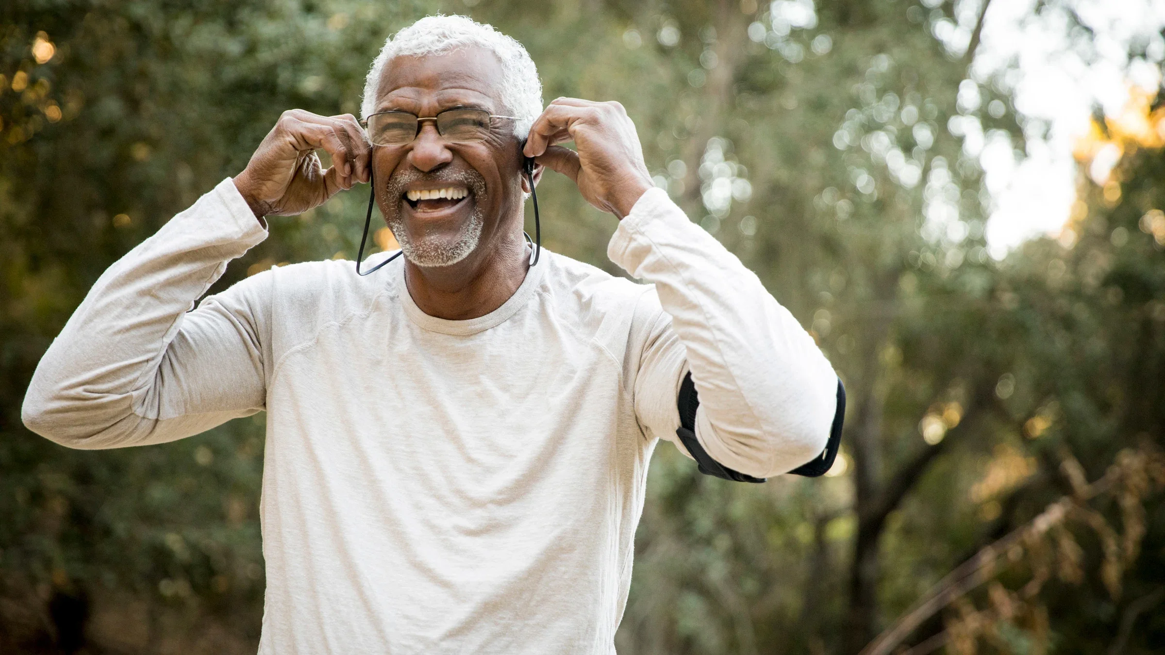 Senior man smiling while putting in his headphones during a run on the trail.
adamkaz/E+ via Getty Images