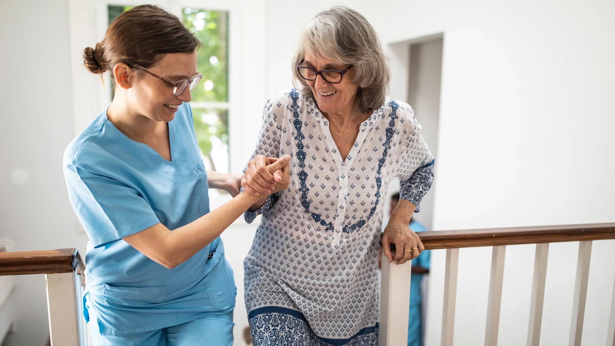 A caretaker helping a senior woman walk up some stairs.