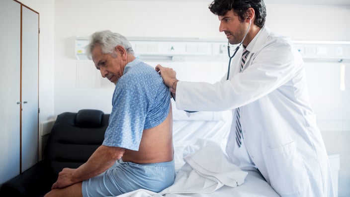 A healthcare professional examines a man’s back. Low back pain is one of the early signs of kidney cancer.