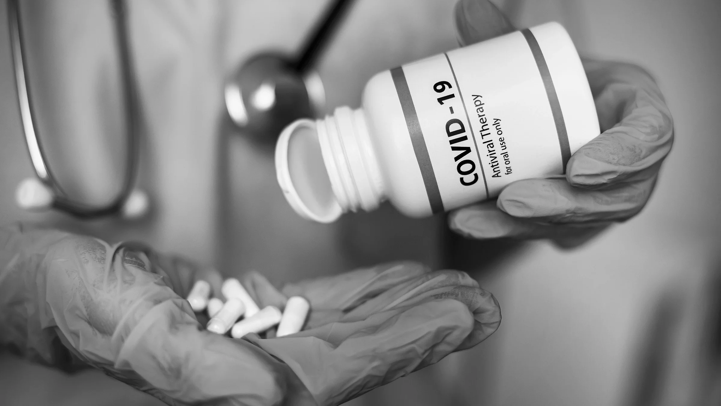 Black and white close-up of a nurse pouring out COVID-19 antiviral pills into their hand.
