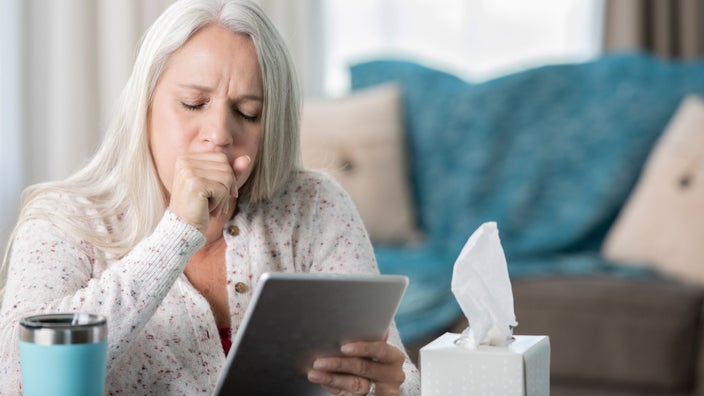 A person with a cough looking something up on their tablet.