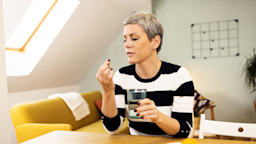 A woman prepares to take a pill with a glass of water.
MixMedia/E+ via Getty Images