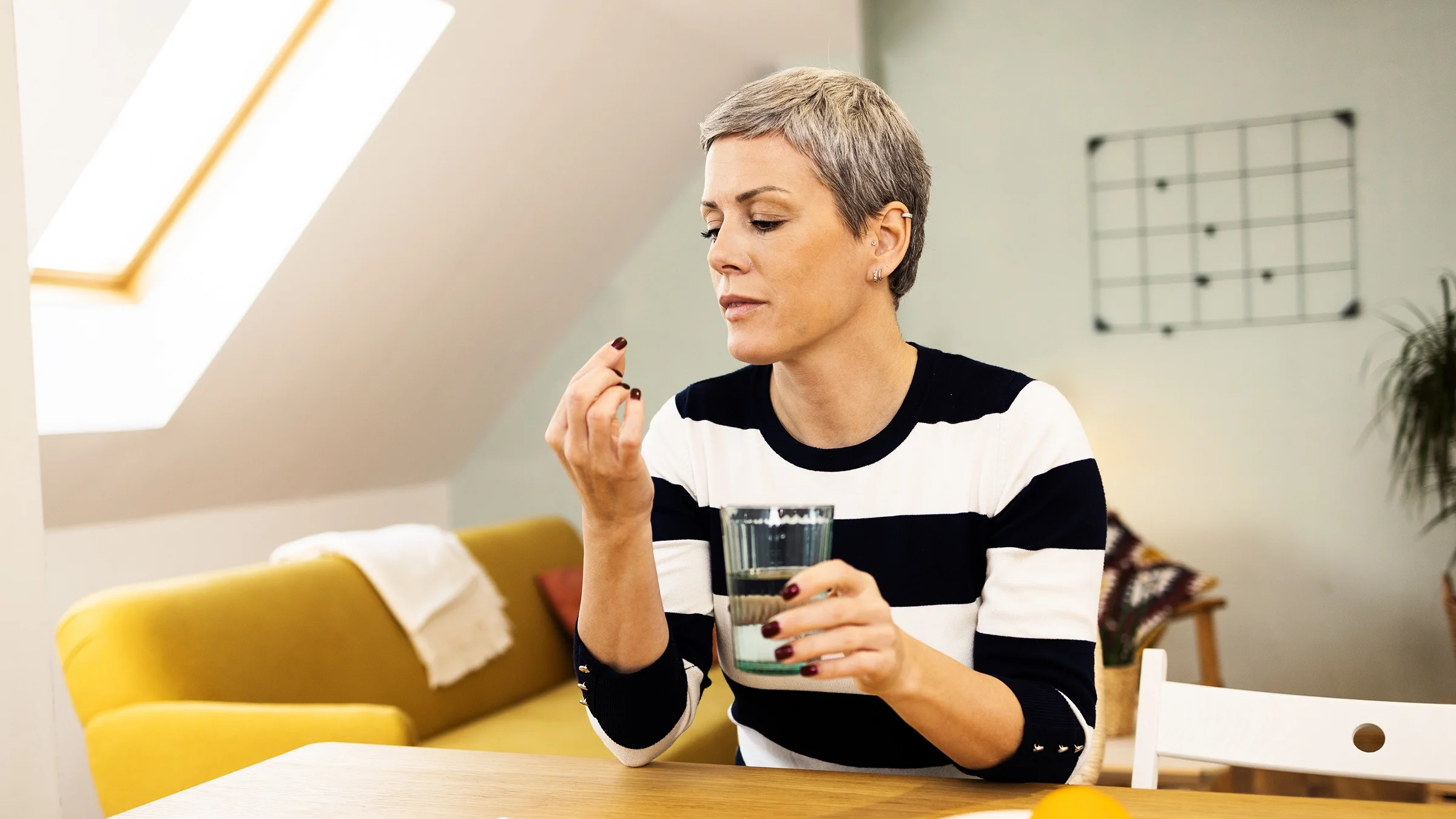 A woman prepares to take a pill with a glass of water.