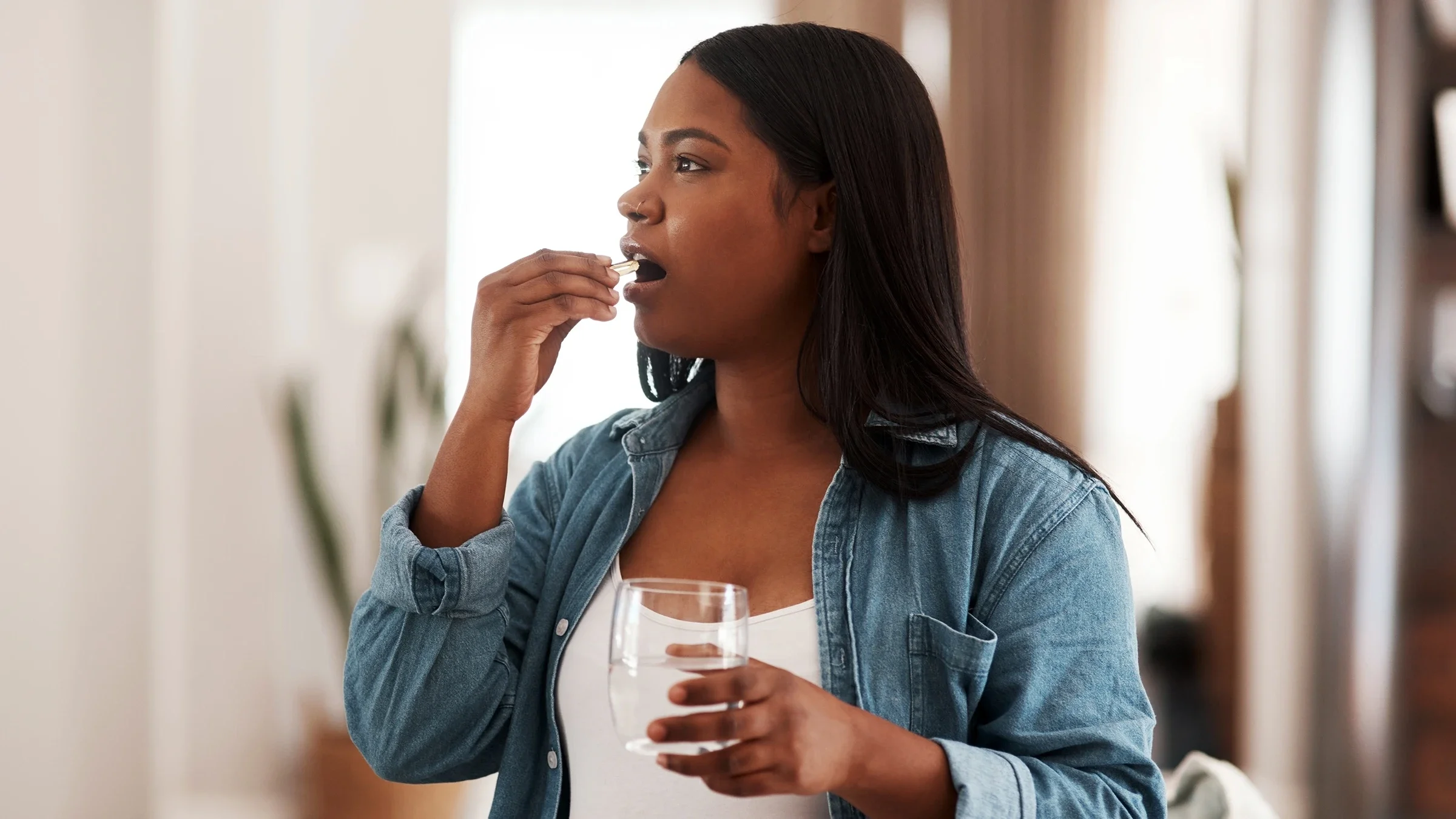 A woman is taking a supplement with a glass of water.