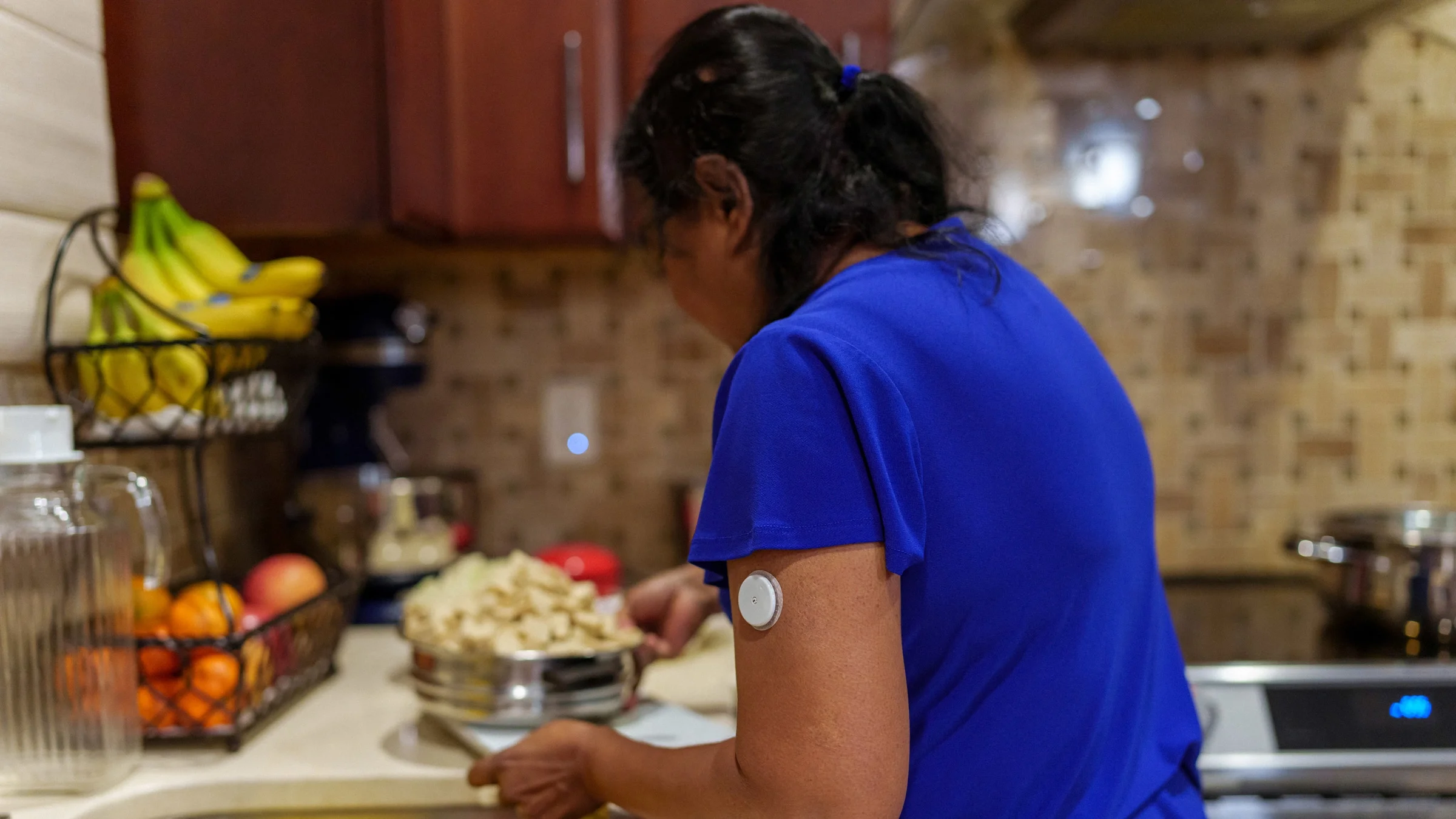 A person cooking in their kitchen, wearing a glucose monitor on their arm.