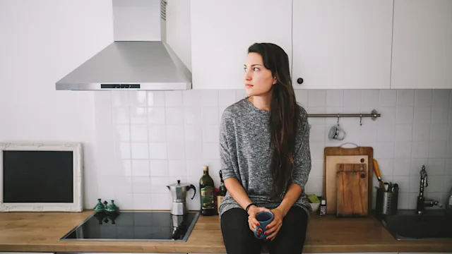 Mental-health: woman sitting alone in the kitchen 1083865112