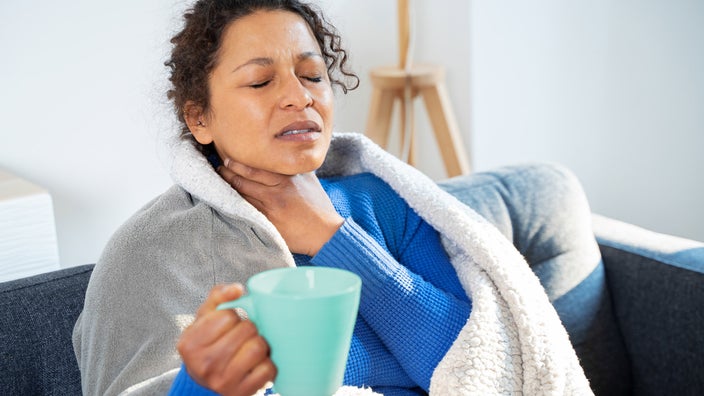 A person soothing their sore throat with tea.