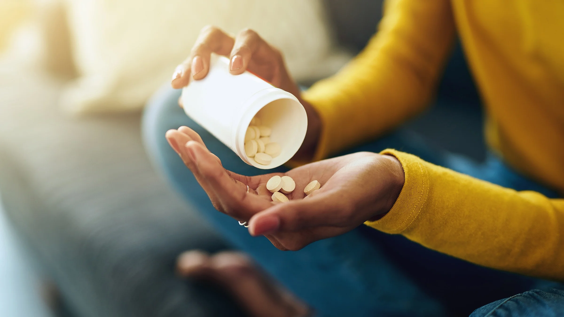 Close-up on a woman pouring yellow pills into her hand.