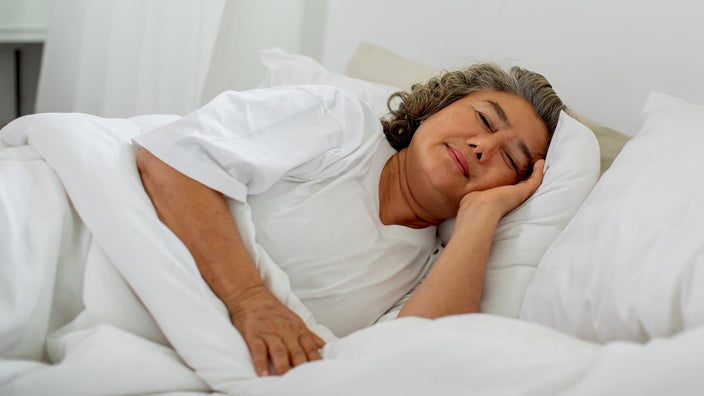 Older woman sleeping in her white sheets.