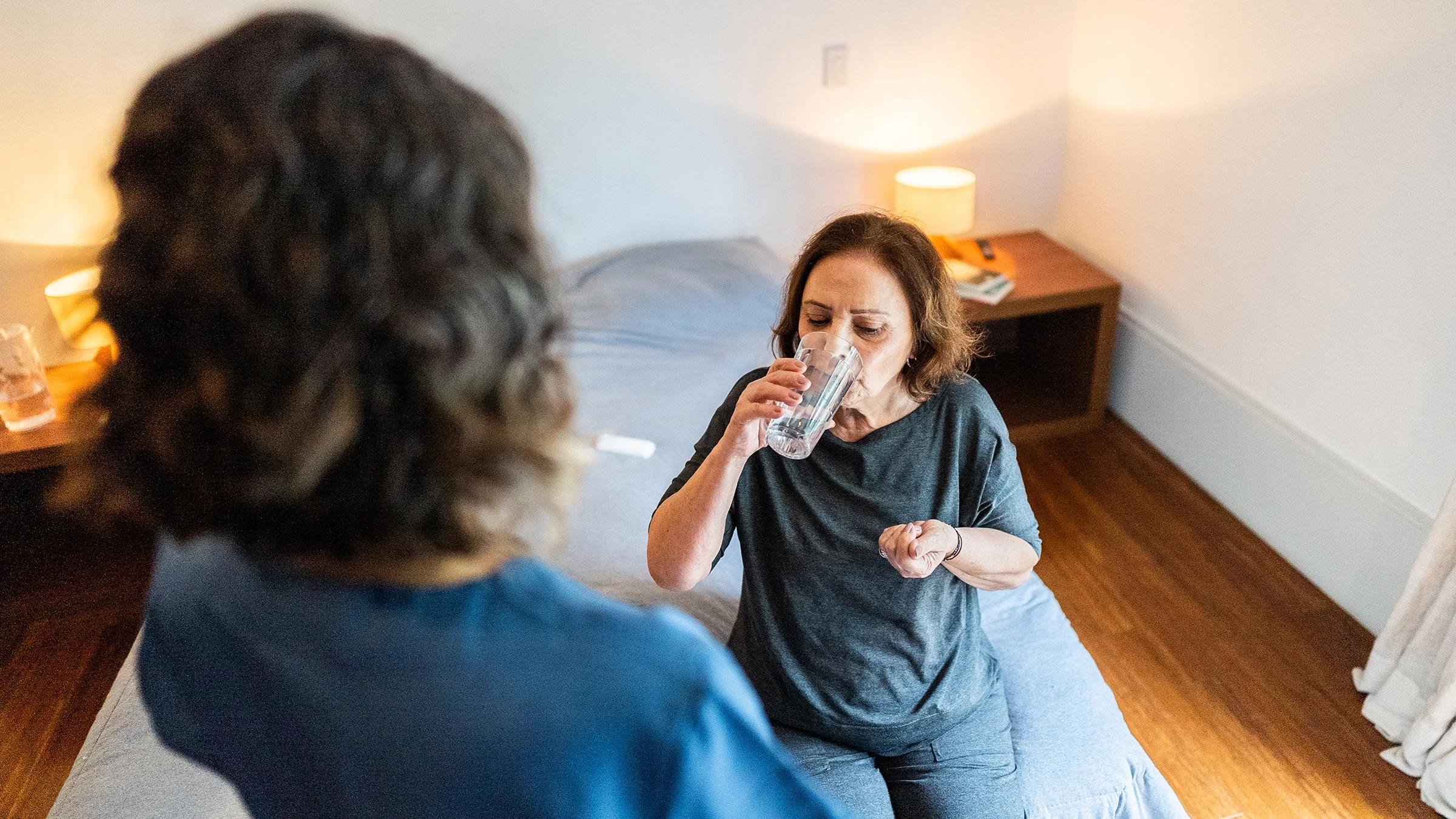 An older woman is taking medication at home with the help of a nurse.